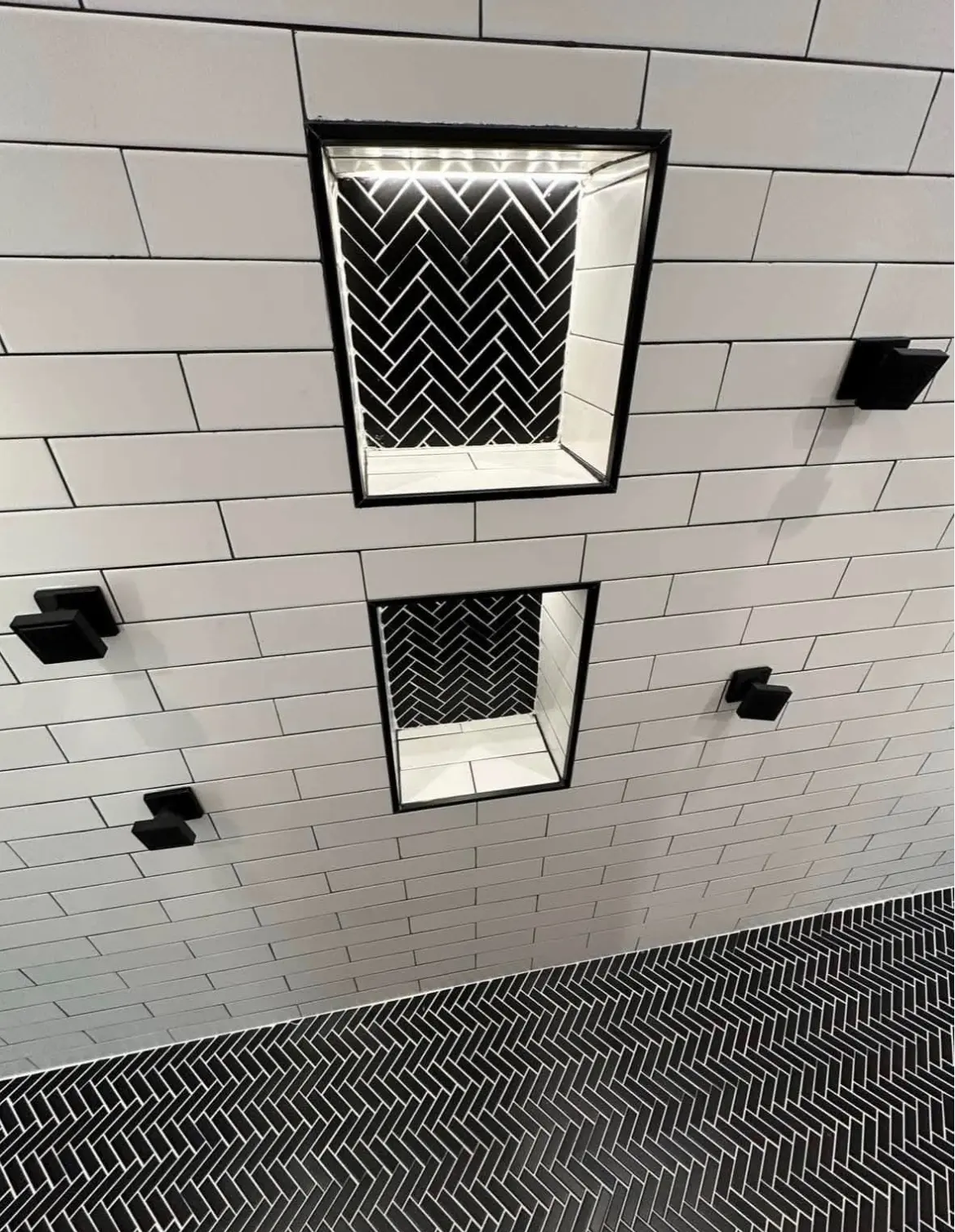 White subway tile shower with lighted herringbone niches and black fixtures