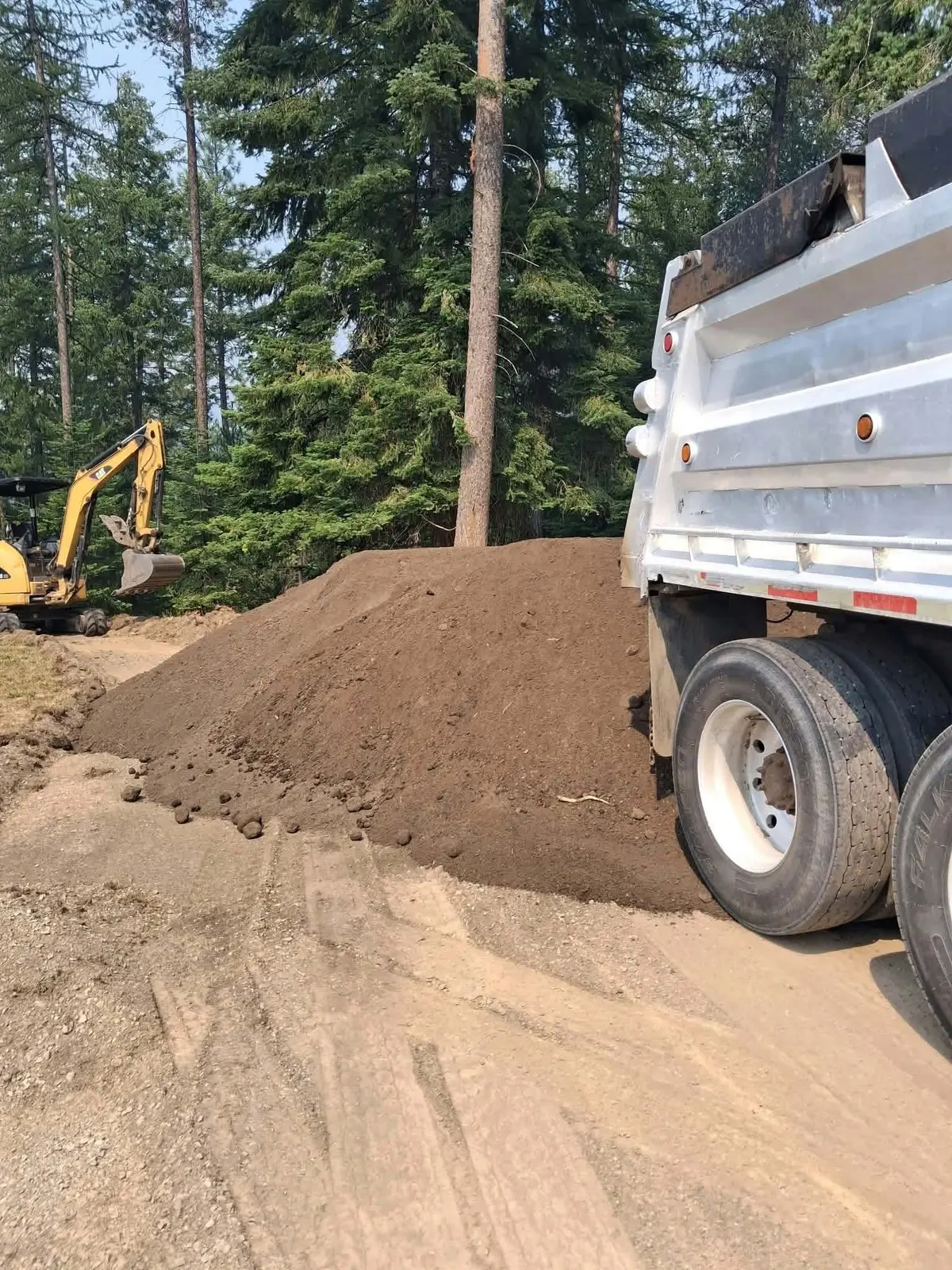 Rustic Ridge dump truck unloading fill dirt on a wooded job site